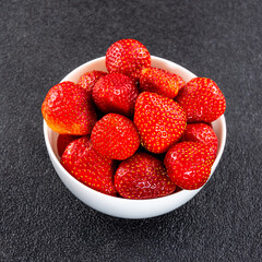 A lot of fresh strawberries in a white vase on a black background close-up