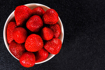 A lot of fresh strawberries in a white vase on a black background close-up