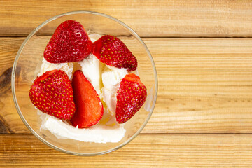 Fresh strawberries with ice cream in a glass vase on a wooden background close-up. Top view. Copy space
