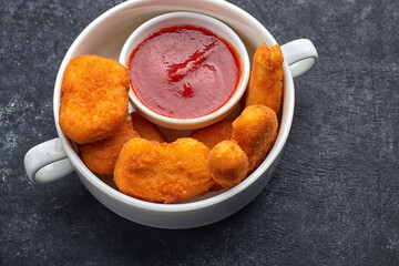 Nuggets in a white deep plate, with sauce inside the plate, on dark concrete