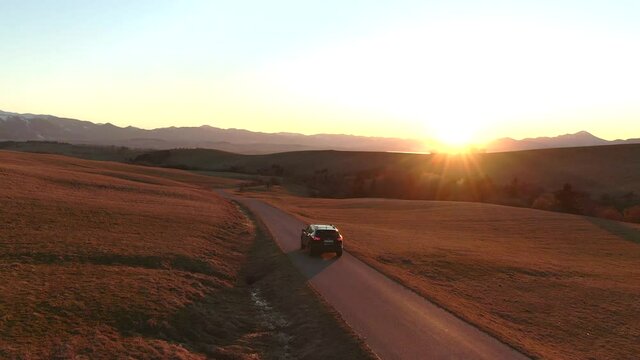 4K aerial drone shot sun flare - lonely car in empty road on the way for a vacation to the lake during a beautiful sunset from bird's perspective - nice landscape