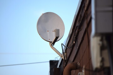 Satellite on the side of business building on a clear summer blue sky day outdoors broadcasting digital data 