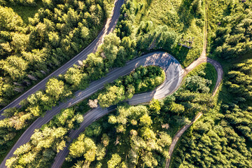 Aerial view of winding road in high mountain pass trough dense green pine woods.