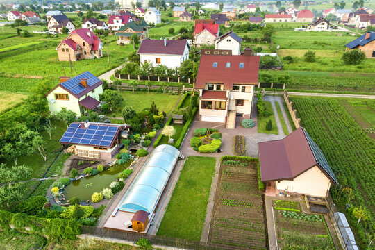 Aerial view of a private house in summer with blue solar photo voltaic panels on roof top and green yard.