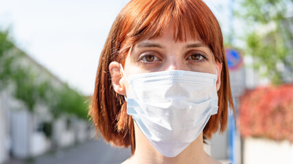 Red-haired girl with surgical mask looks into the camera