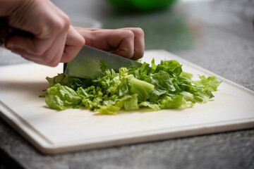 hands cutting lettuce with knife on white table on kitchen counter