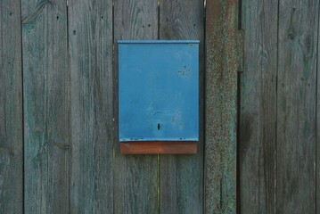 one blue metal mailbox hanging on gray wooden planks of fence wall