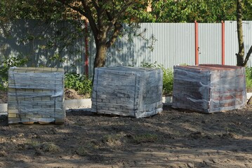 three square boxes in plastic packaging with paving bricks stand on gray ground outside