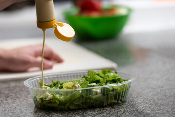hand putting ingredients into a salad on plastic tray for delivery