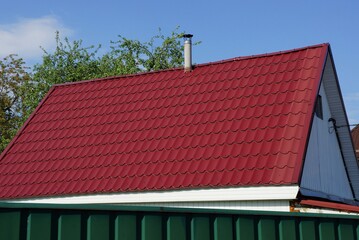 the attic of a private house under a red tiled roof with a chimney against a blue sky on a sunny day