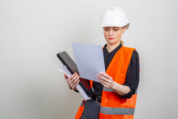 A girl in a construction helmet and a bright vest. The girl works in a construction company. A woman reads construction documents. Engineer of safety engineering
