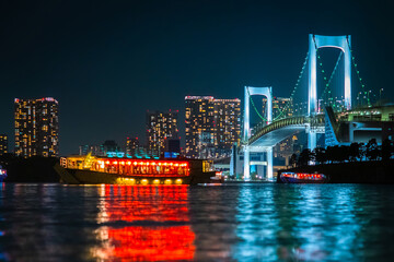 Fototapeta na wymiar Japan. Evening in Tokyo. A pleasure ship sails through Tokyo Bay. Water evening walk on Tokyo Bay. Rainbow bridge in the evening. The island of Odaiba in the dark.