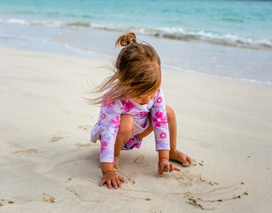 Young girl in flower swimsuit plays in sand at beach