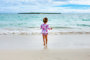 Young girl in flower swimsuit runs down beach to the ocean