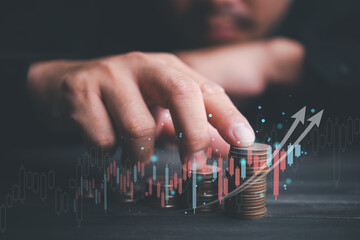 Investment business Finance concept.Money management and Financial chart. Businessman is touching a growing virtual hologram stock and rows of coins on dark tone background.Business stock analysis.