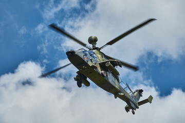 Fototapeta na wymiar Green military helicopter in flight in front of a blue sky with clouds.