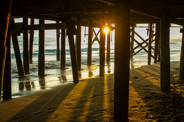 Sunset from under a pier with surf sand waves and surfers out in the water