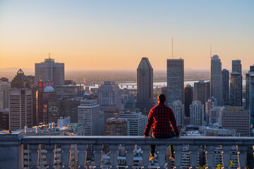Montreal, Canada - may 2020 : back view of a young man wearing a lumberjack shirt, admiring the sunrise from the Kondiaronk belvedere   - obrazy, fototapety, plakaty