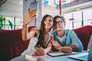 Cheerful young man and woman watching funny webinar on netbook in cafe