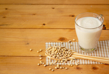 Soy milk in glass and soy bean on spoon it on wooden table background, healthy concept
