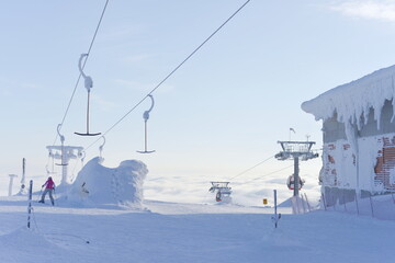 Fototapeta na wymiar At the top of ski lifts as they rise above the clouds, covered in snow, only 1 skier