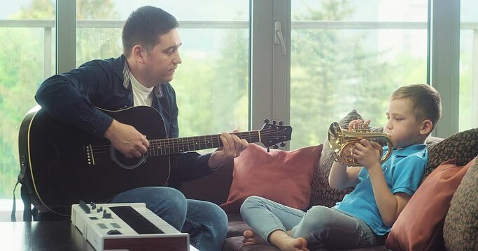Father and son playing guitar and trumpet at home. Dad teaches child to play musical instruments. Music hobby, Create, learning own songs. 4K video. 