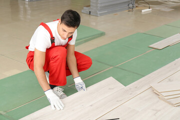 Carpenter installing laminate flooring in room