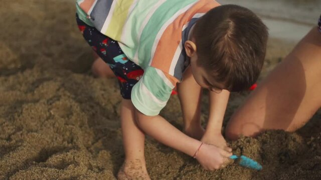 Caucasian mother and son digging the sand at beach of Schinias, Marathonas, Greece. Close up shot