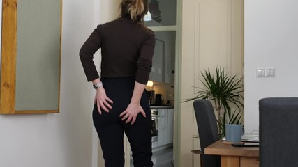 Young tall woman feels sudden pain in the anus caused by hemorrhoids, touches her buttocks. Medium shot