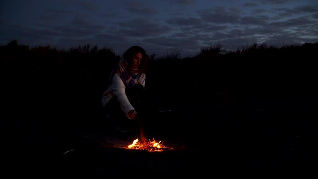 Young girl alone in dark woods alone by campfire