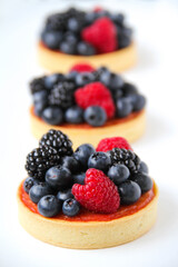 French dessert. Three berry tarts are decorated with organic fresh blueberries, raspberries and blackberries. White background. Back view. 