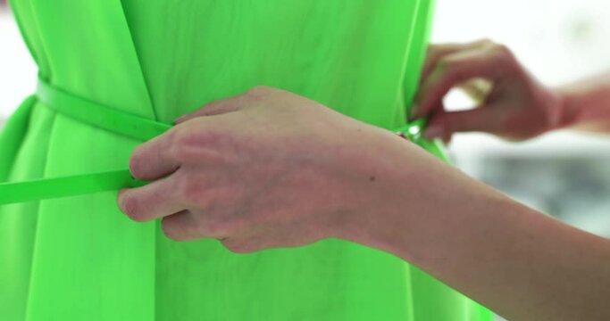 Female hands fasten a belt on a light green blouse on a mannequin in the studio