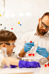 dad and son the child stayed at home conduct experiments on a white table, behind them on the wall is a white Board magnetic-marker