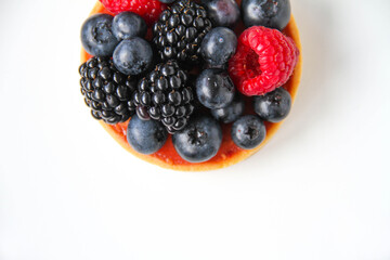French dessert. Half of a berry tart decorated with organic fresh blueberries, raspberries and blackberries. White background. Top view.  There is a copy space for your text.