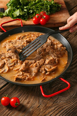 Woman cooking tasty beef stroganoff on table