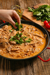 Woman cooking tasty beef stroganoff on table