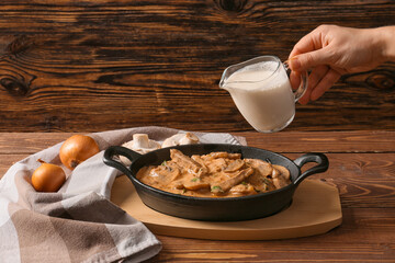 Woman cooking tasty beef stroganoff on table