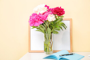 Vase with beautiful peony flowers and notebook on table in room
