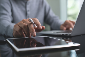 Casual man working on digital tablet and laptop computer at home office