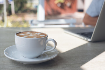 Cup of coffee on table with man working on laptop computer as background