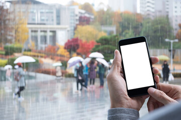Mockup of man using mobile phone with blurred people walking in the rain 