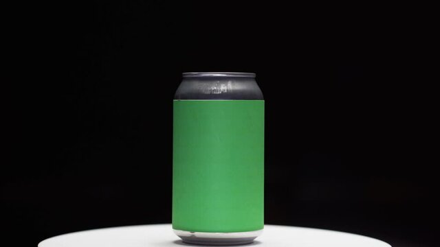 Soda or beer can with chroma green screen label spinning on turntable stand in studio with black background zoom in