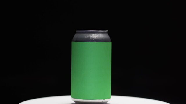 Hand setting down soda or beer can with chroma green screen label on stand in studio with black background zoom in