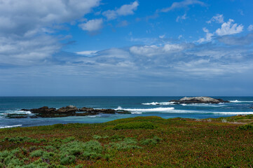 Rocky blue Pacific ocean coastal landscape with waves breaking against the rocks under a dramatic partly cloudy sky