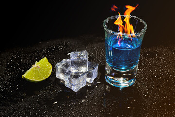 Cocktail blue burning in shot glass  with salt and lime, ice cubes on black background.