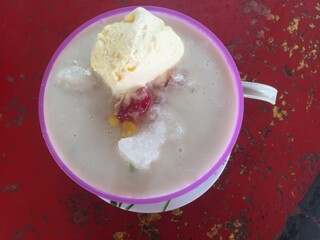 Top view Special iced cendol or Malaysian called cendol pulut special with sticky rice,cendol,corn,peanuts,red beans and vanila ice cream on red table