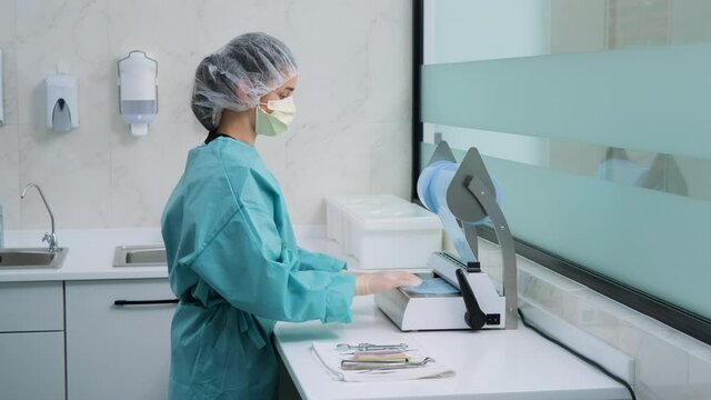 Laboratory technician in white gloves and green gown cuts off packaging for dental tools for further disinfection in autoclave. Dentist prepares instrument for sterilization