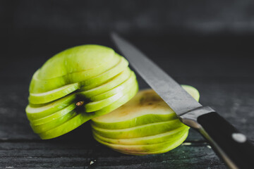 food ingredients concept, green apple cut into thin equal slices stacked into two halves with knife