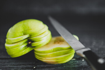 food ingredients concept, green apple cut into thin equal slices stacked into two halves with knife