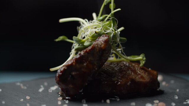 Close up of beef steak with microgreen and salt rotating on black background in slow motion. Two pieces of filet mignon